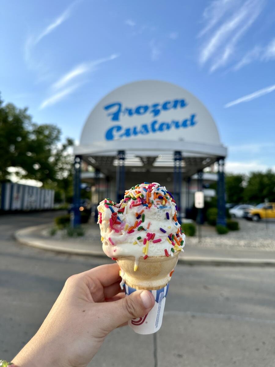 A frozen custard cone held in front of the Igloo Frozen Custard sign